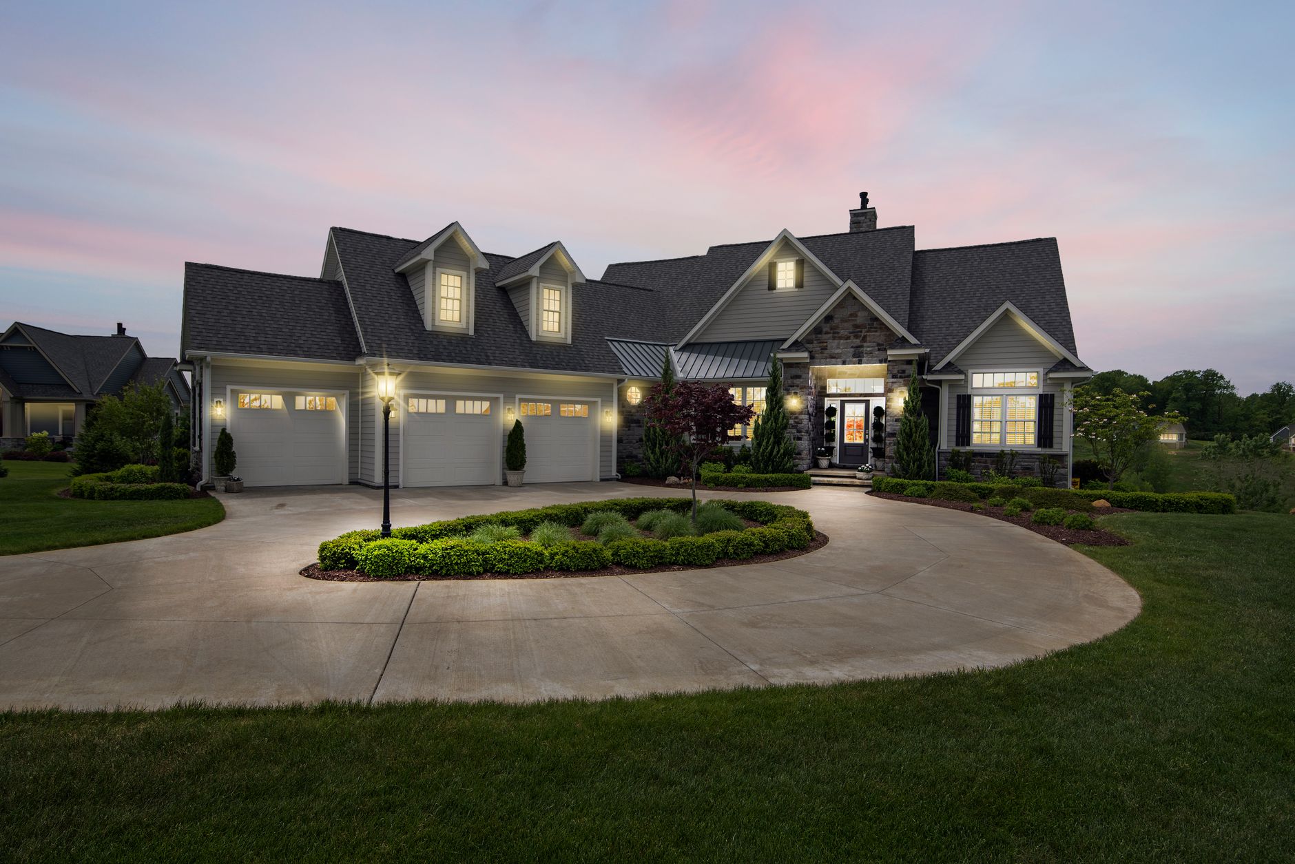 Two story home at dusk with lit windows and a curved driveway