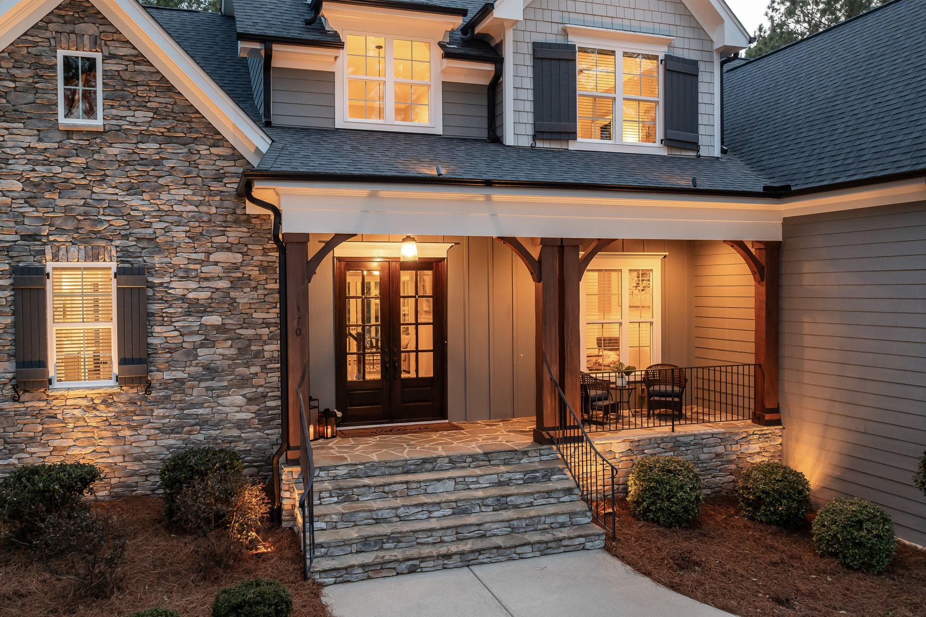 Covered stone entry of a home with warmly lit windows in the evening